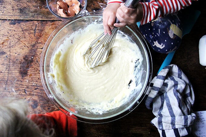 Two children whisking the batter of a one-bowl buttermilk birthday cake sitting on top of a table.