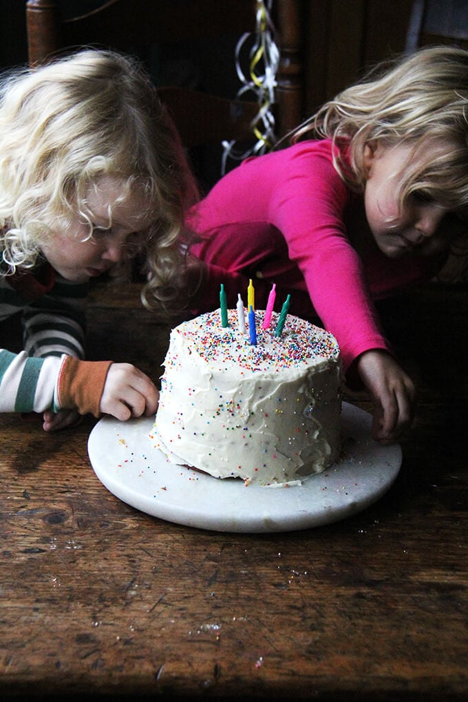 Wren and tig going after sprinkles around the assembled one-bowl buttermilk birthday cake.