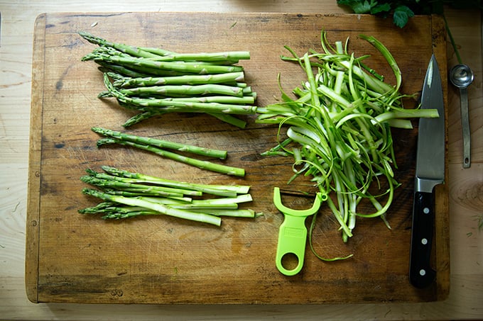 A cutting board with asparagus, shaved with a peeler.