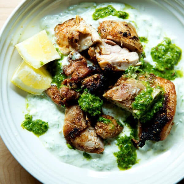 A platter of grilled, smokey chicken, cucumber-yogurt sauce,, skhug and lemon