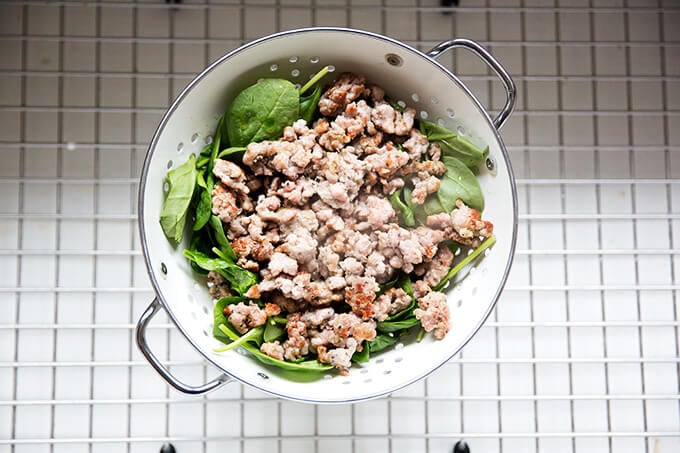 Sausage and spinach in colander in sink.