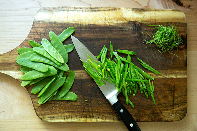 Slivered snow peas on a cutting board with a knife.
