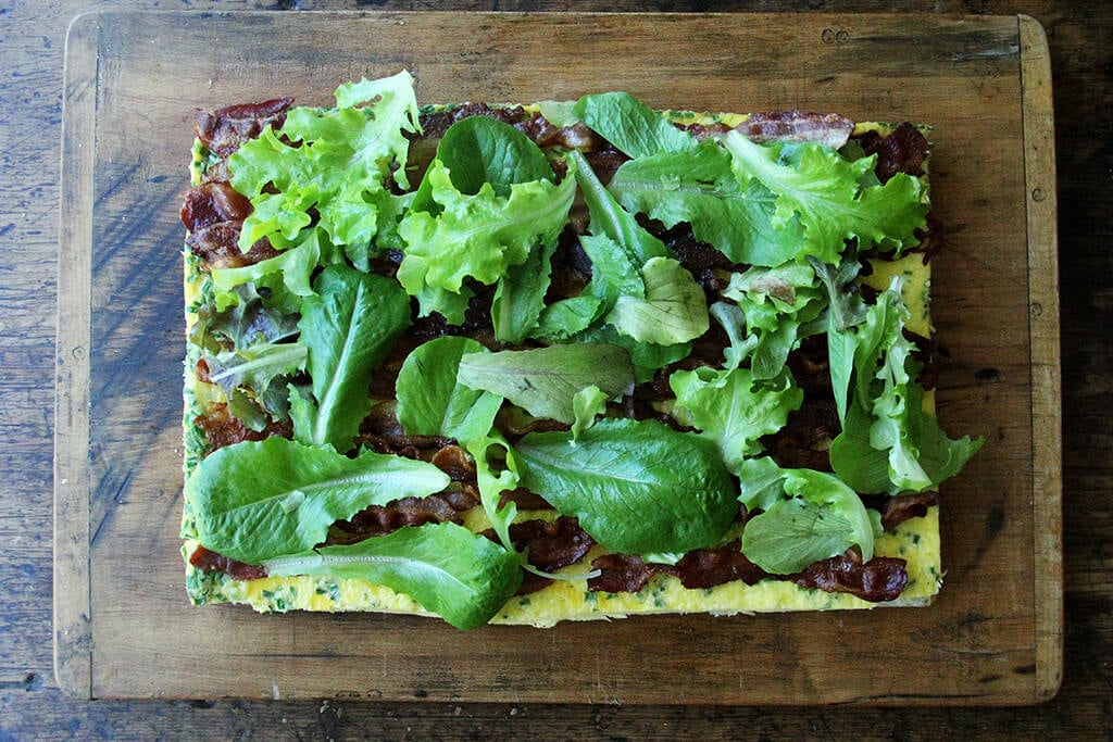 A cutting board with the sheet pan breakfast sandwich being assembled.