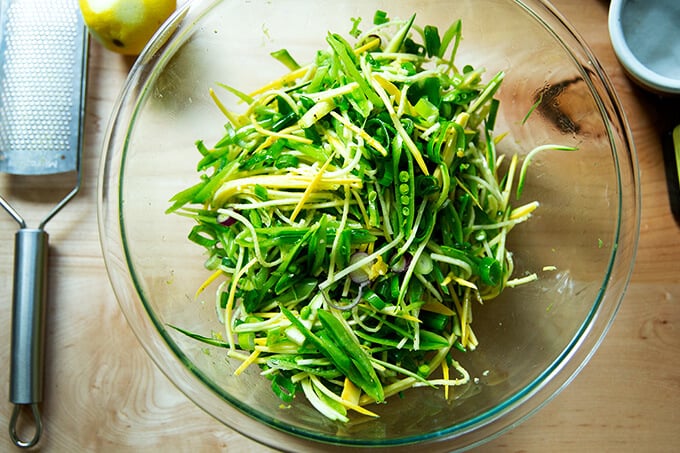 A bowl with slivered snap peas, summer squash and spring onions all tossed together.