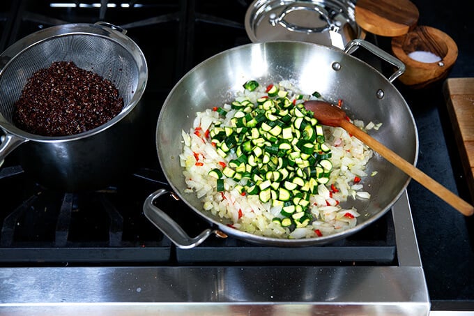 A sauté pan filled with onions, chili, and zucchini.