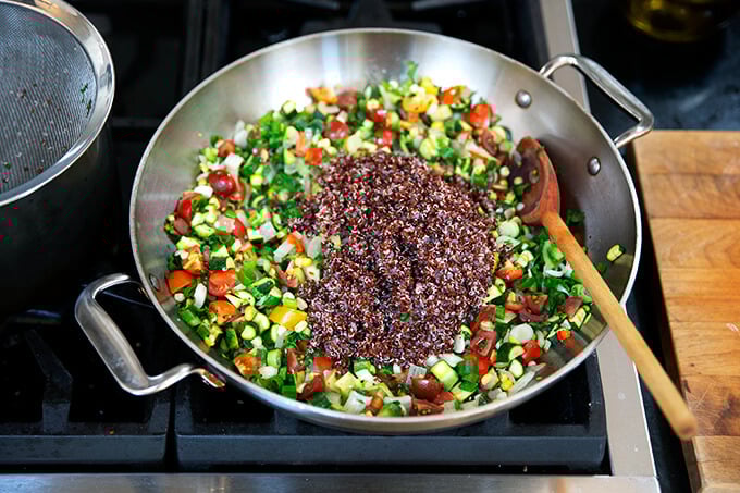 A sauté pan filled with onions, chili, zucchini, corn, and quinoa.