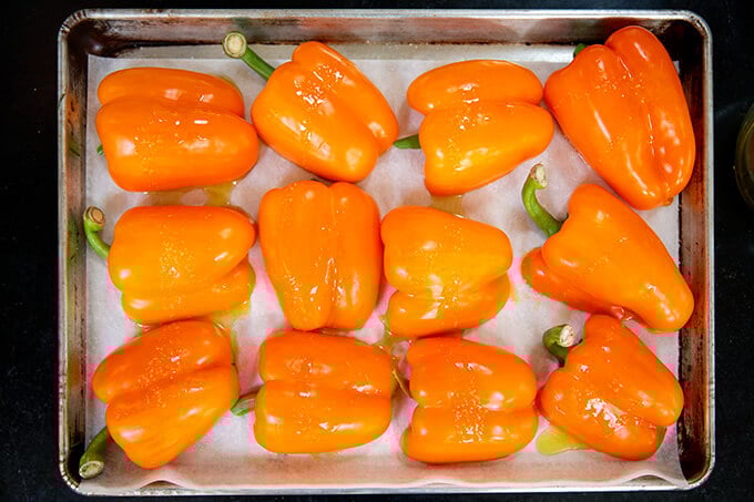 A sheet pan of halved orange bell peppers cut side down.