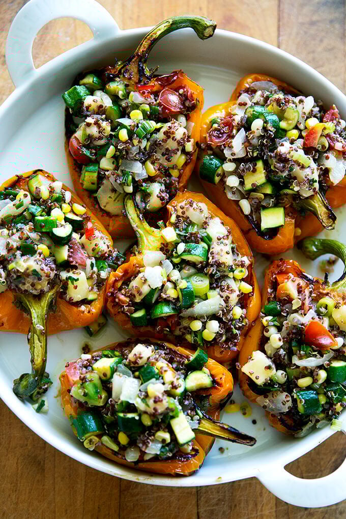 A round white dish filled with orange bell peppers stuffed with quinoa, vegetables, and Monterey Jack cheese.
