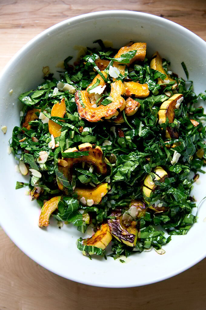 A large bowl filled with raw collard greens salad tossed with roasted delicata squash.