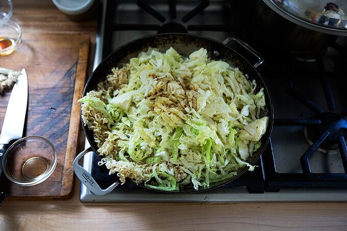 A large sauté pan filled with mushrooms, ginger, cabbage, and noodles.