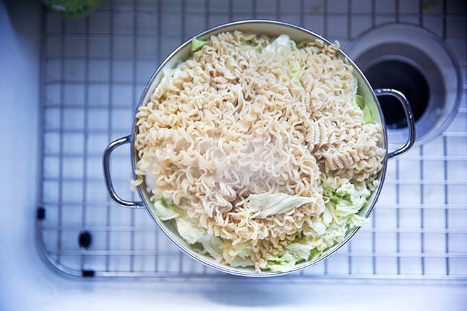 An overhead shot of a colander standing in a sink filled with finely shredded cabbage and cooked ramen noodles.