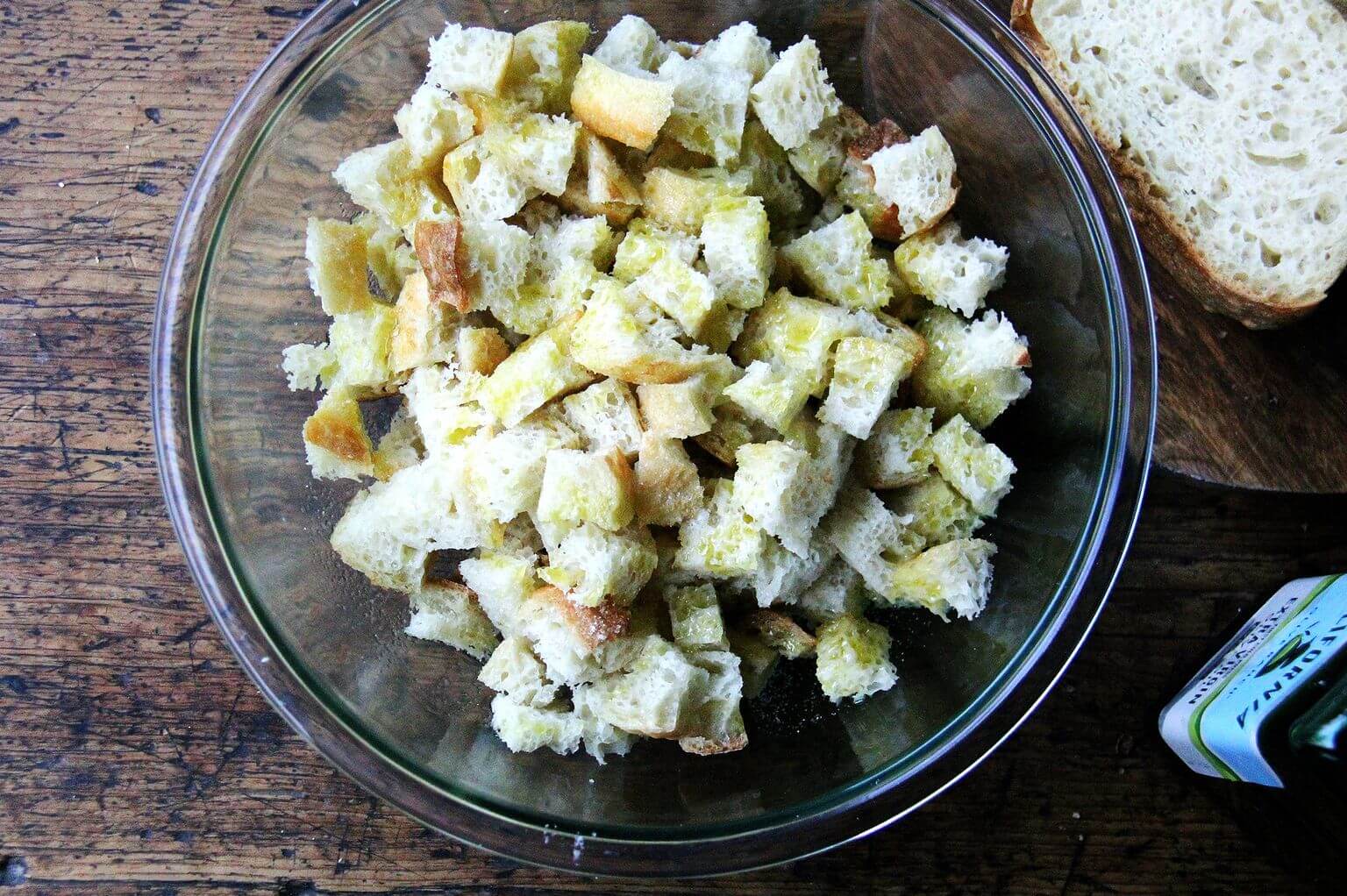 An overhead shot of a bowl of cubed peasant bread tossed with olive oil.