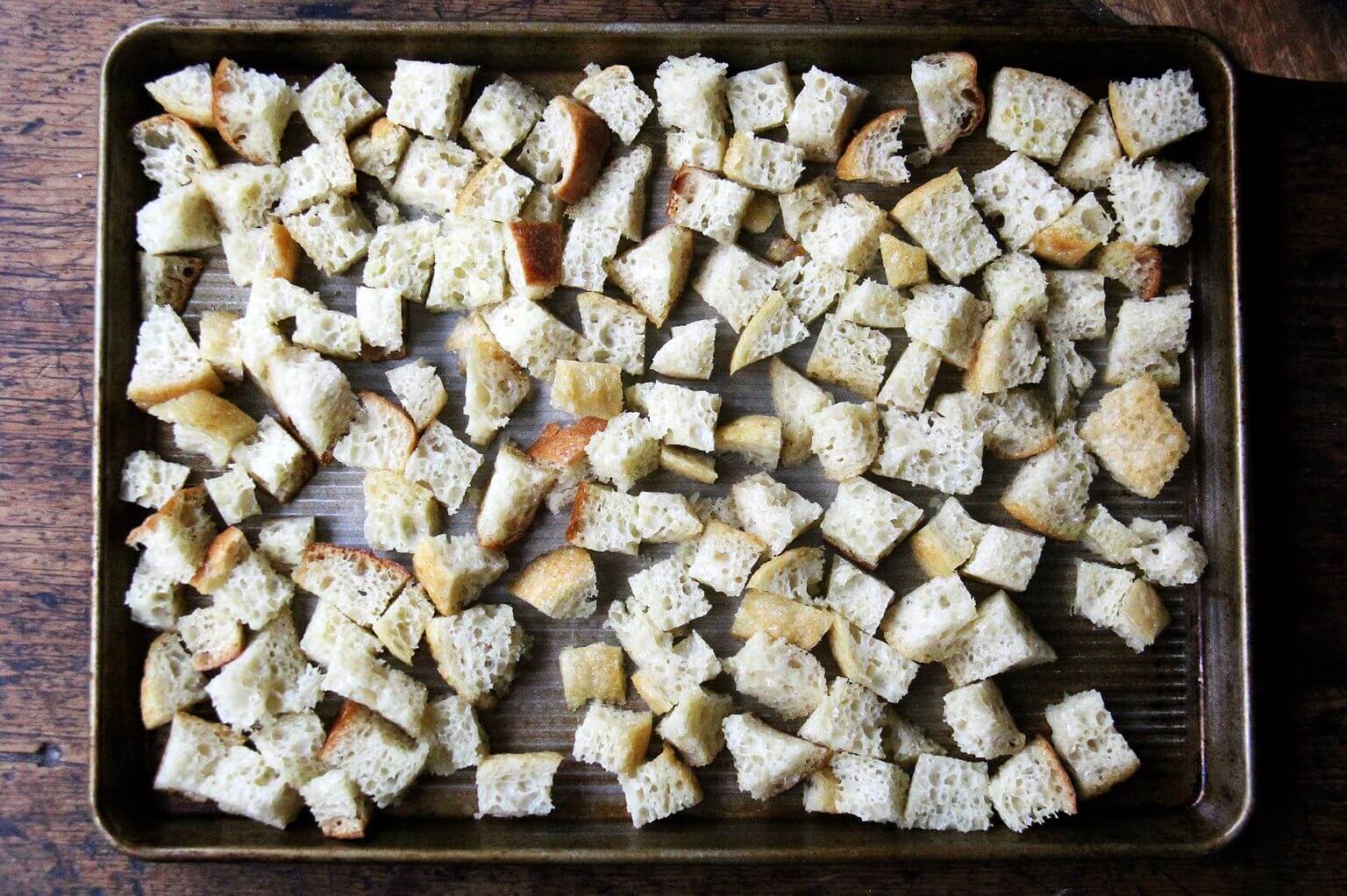 A sheet pan with cubed peasant bread tossed in olive oil.