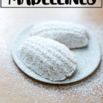 Lemon madeleines dusted in powdered sugar on a cooling rack.