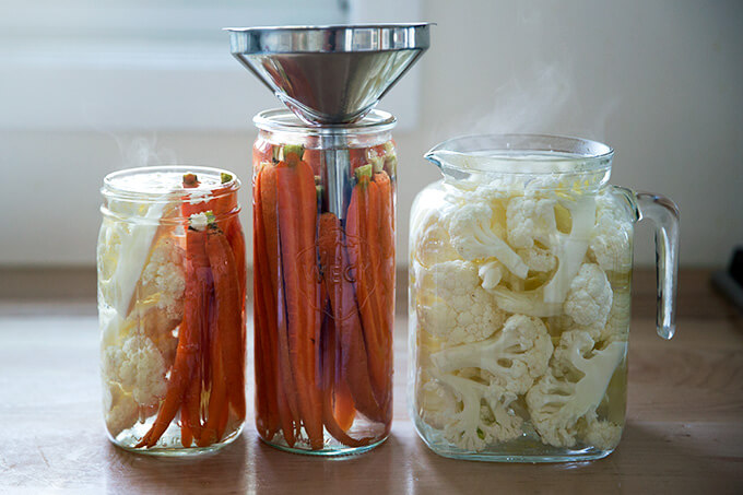 Pickled cruditรฉ in glass jars, one with a funnel.