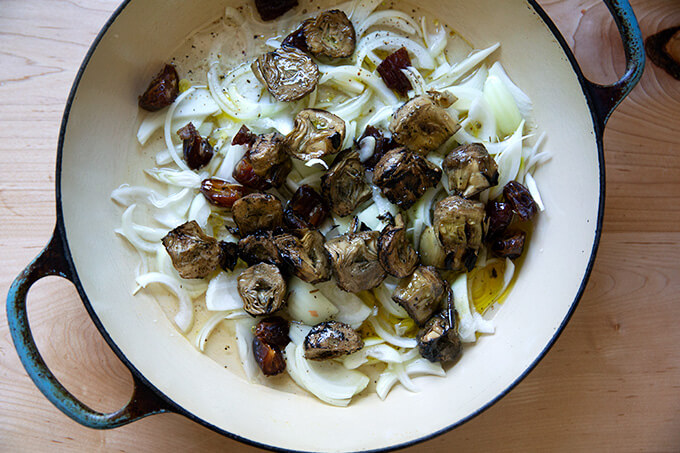 A skillet filled with onions, artichoke hearts, and dates.