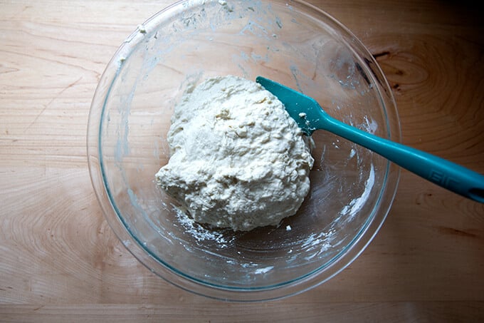 Sourdough pizza dough, just mixed, in a glass bowl with a spatula.
