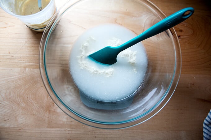A bowl on a scale with a spatula and water, sourdough starter, and salt.