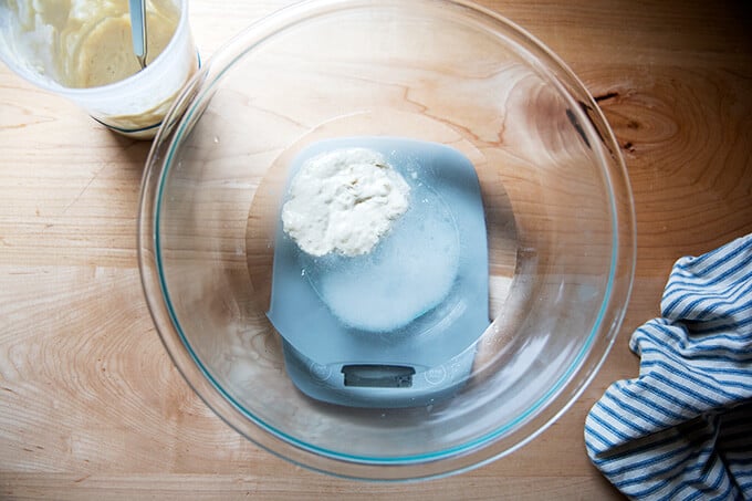 A bowl filled with water, sourdough starter, and salt on a scale.