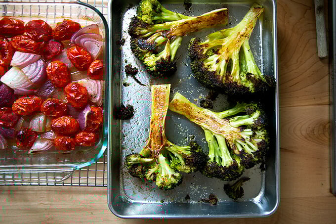 Two pans: one holding roasted tomatoes and onions; the other holding roasted broccoli.