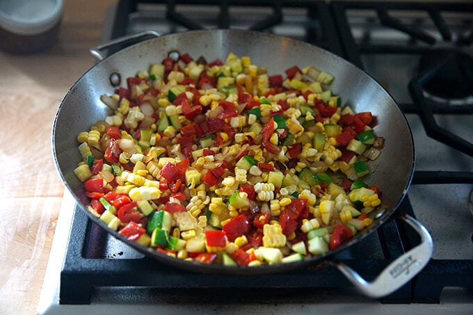 A skillet on the stovetop with sautéed summer vegetables.