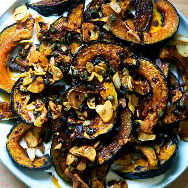 A plate of roasted Kabocha squash atop lemony yogurt sauce and sizzling garlic, capers, and Calabrian chili paste.
