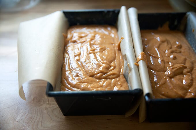 Two loaf pans filled with pumpkin bread batter.