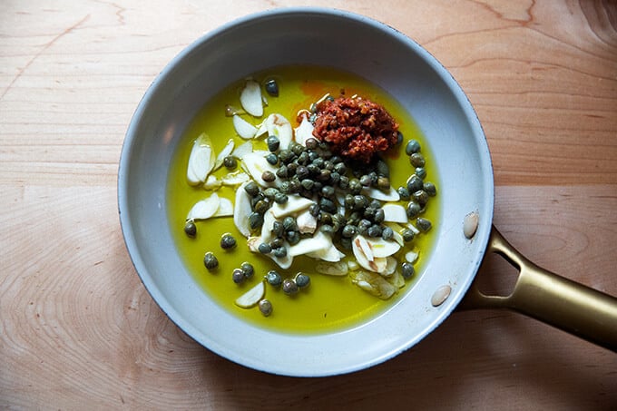 A skillet filled with oil, garlic, capers, and Calabrian chili paste.