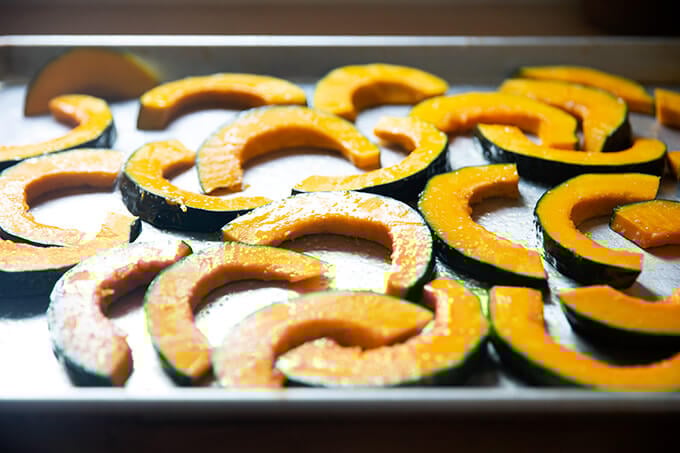 Sliced kobacha squash tossed with olive oil and salt on a sheet pan.