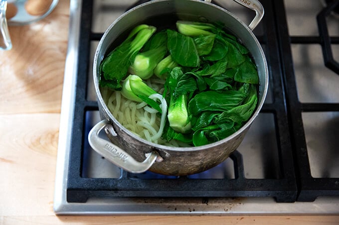 Bok choy and udon noodles in a pot. 