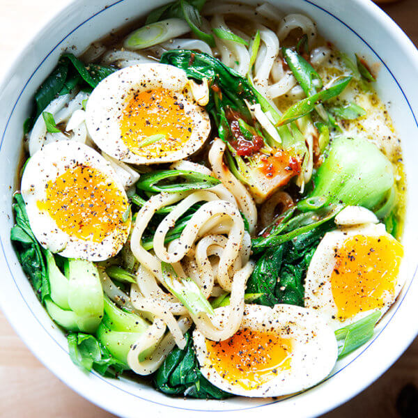 A bowl of udon noodles topped with eggs and hot sauce.