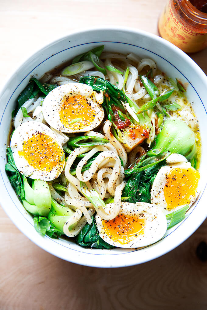 A bowl of udon noodles topped with eggs and hot sauce.