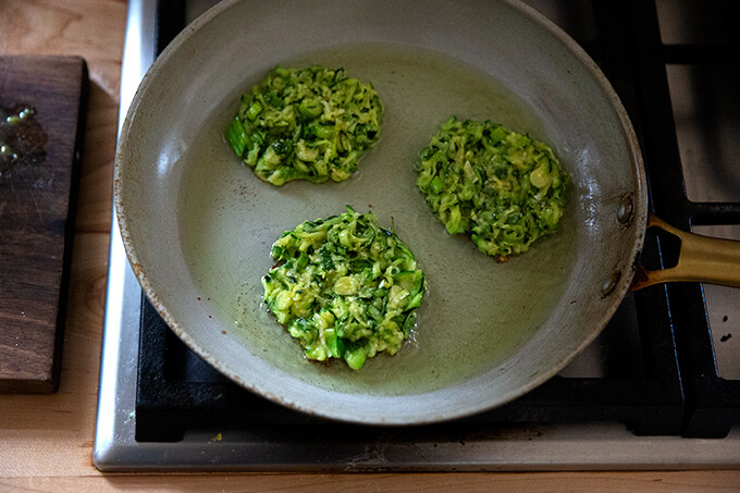 Zucchini fritters frying in a frying pan.