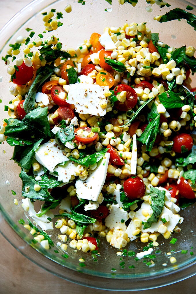 A raw corn salad made with tomatoes, feta, and lots of herbs all tossed together in a bowl.