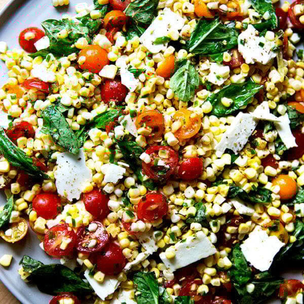 A platter topped with a raw corn salad made with tomatoes, feta, and lots of herbs.