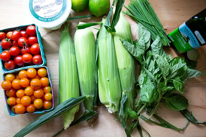 The ingredients to make a raw corn, tomato, and feta salad on a countertop.