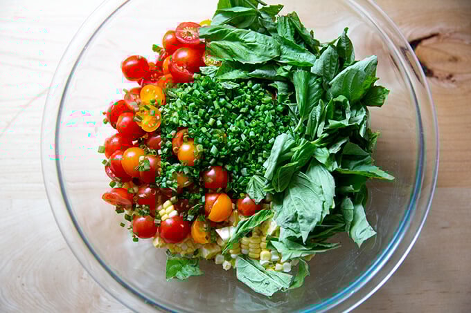 A bowl filled with the ingredients to make a raw corn salad made with tomatoes, feta, and lots of herbs.