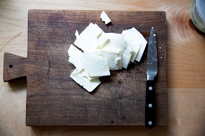 Sliced feta on a small, wooden cutting board.