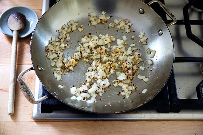 A skillet holding onions, garlic, ginger and crushed red pepper flakes.