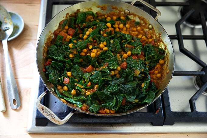 A skillet holding curry spiced chickpeas, kale, and tomatoes.