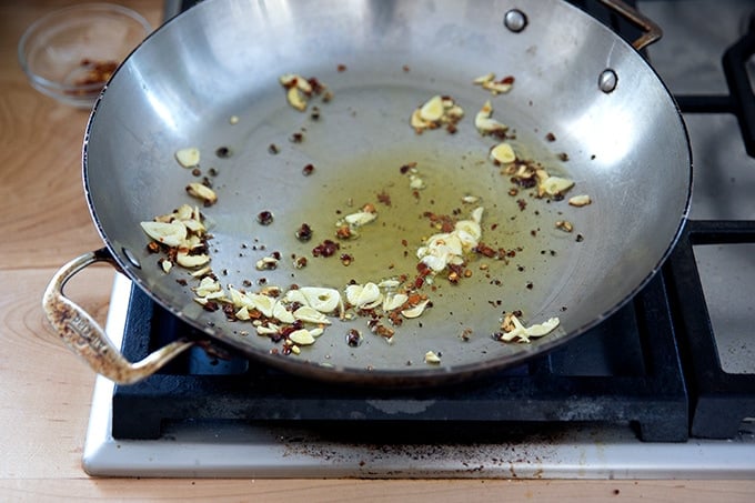 A large skillet stovetop with some olive oil, slice garlic, and crushed red pepper flakes inside.