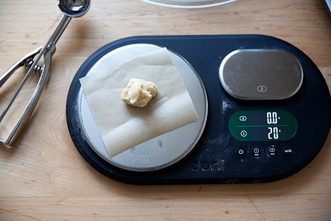 A scale holding a 20-gram portion of lemon-almond snowball cookie dough.