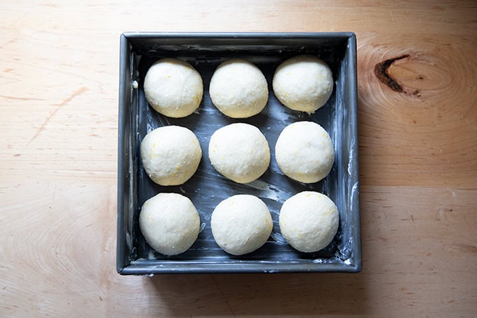 A 9-inch square pan filled with 9 dough balls of hot cross buns.
