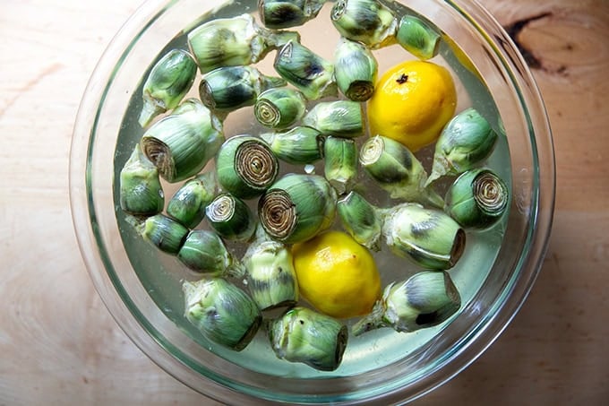 A large bowl filled with water, lemon, and baby artichokes cleaned and trimmed.