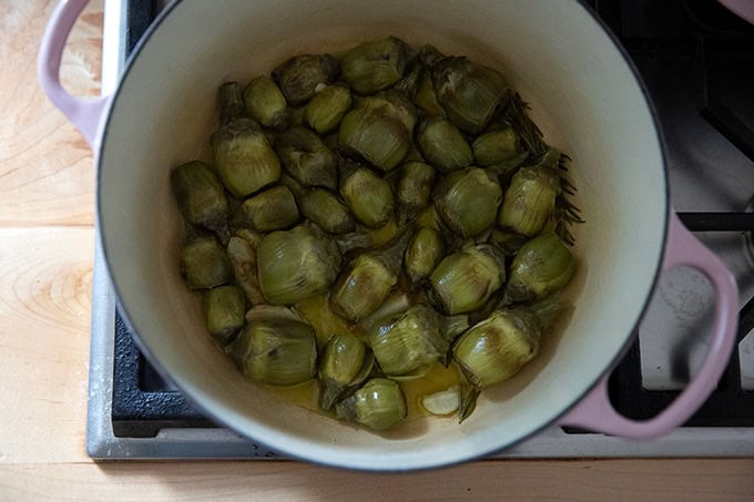 A large pot on the stovetop filled with baby artichokes halfway through their cooking process.