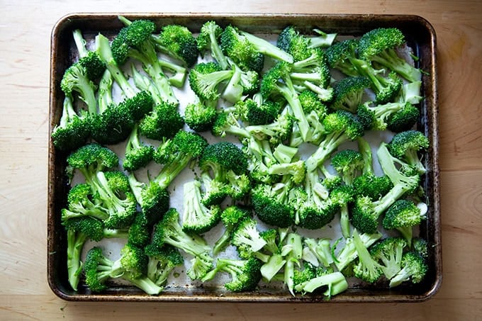 A sheet pan filled with broccoli florets tossed with sliced garlic, olive oil, salt, and pepper.