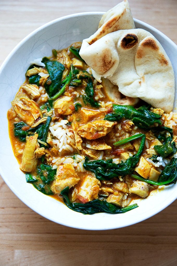 A bowl of butter chicken with spinach, rice and naan.
