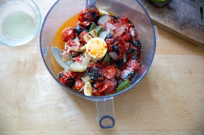 A food processor filled with broiled tomatoes, onions, garlic, and jalapeños along with a pinch of salt and fresh lime juice.