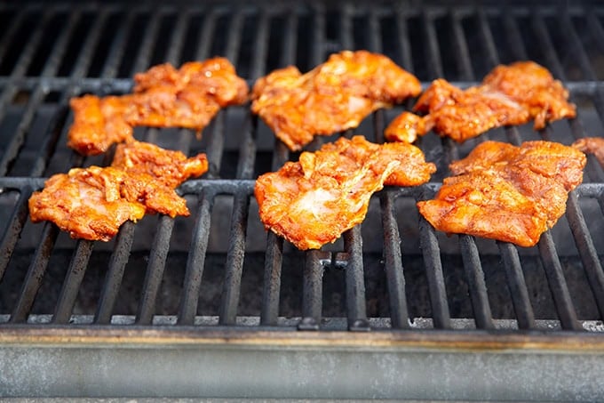 Six chicken thighs on a gas grill.