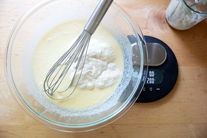 A large bowl on a scale filled with the wet ingredients to make sourdough discard pancakes.